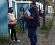 servidores entrevistam pessoas na fila para receber o kit merenda escolar