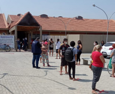 servidores entrevistam pessoas na fila para receber o kit merenda escolar