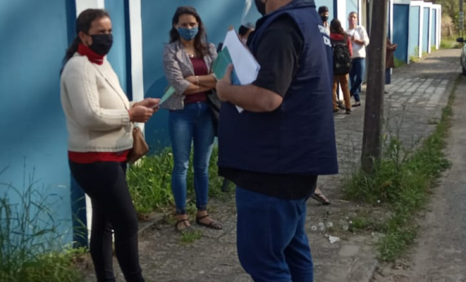 servidores entrevistam pessoas na fila para receber o kit merenda escolar