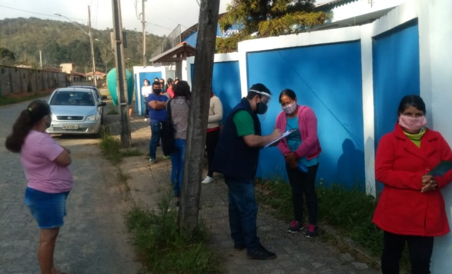 servidores entrevistam pessoas na fila para receber o kit merenda escolar