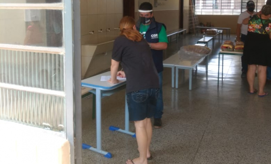 servidores entrevistam pessoas na fila para receber o kit merenda escolar