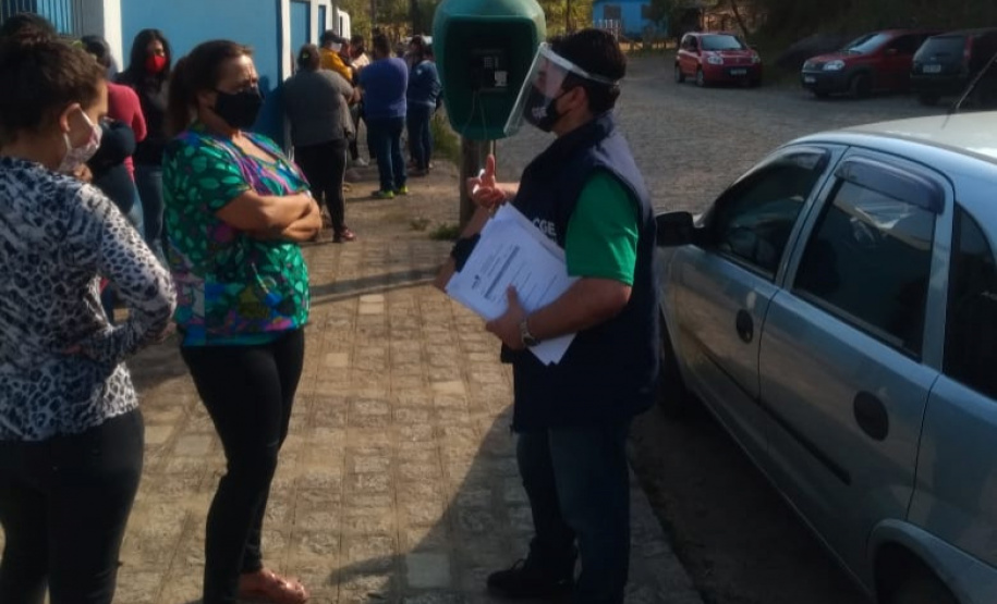 servidores entrevistam pessoas na fila para receber o kit merenda escolar